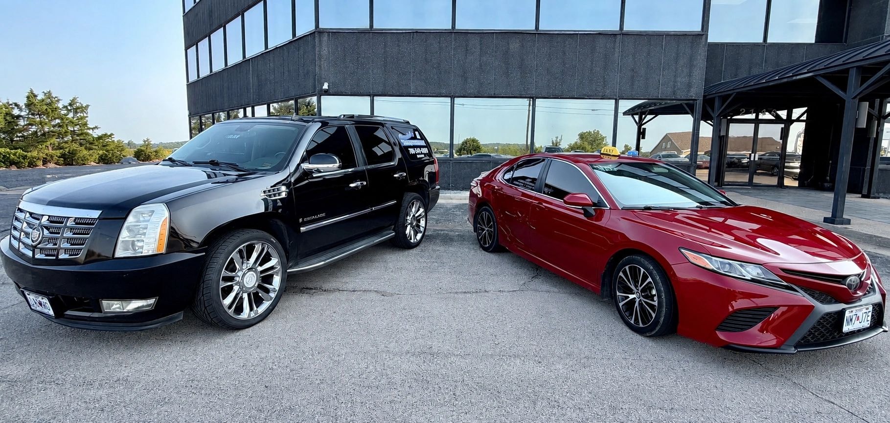 Black Cadillac Escalade and red Toyota Camry parked in front of modern building